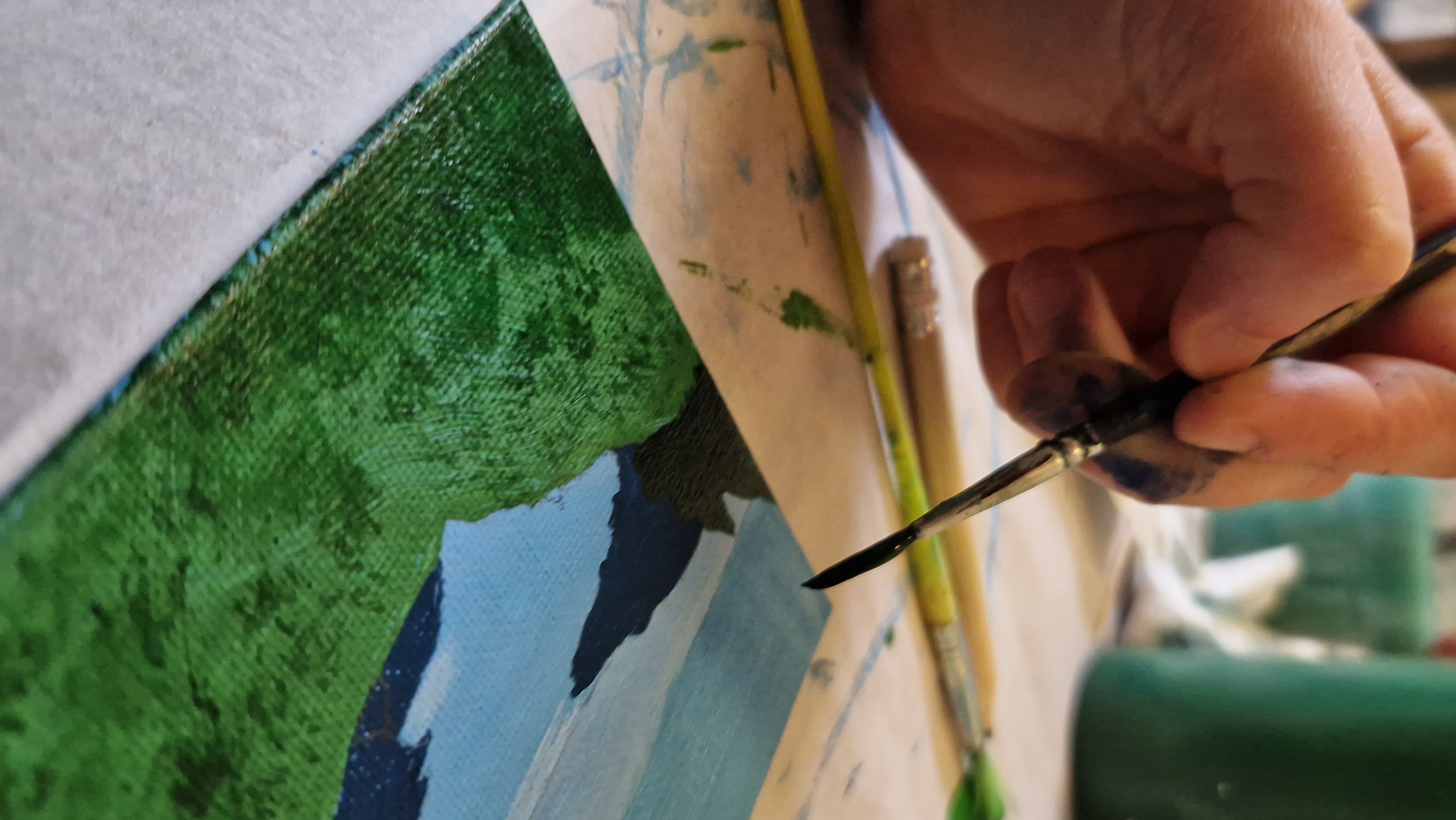 Gros plan d’une main et d’un pinceau sur une toile en cours