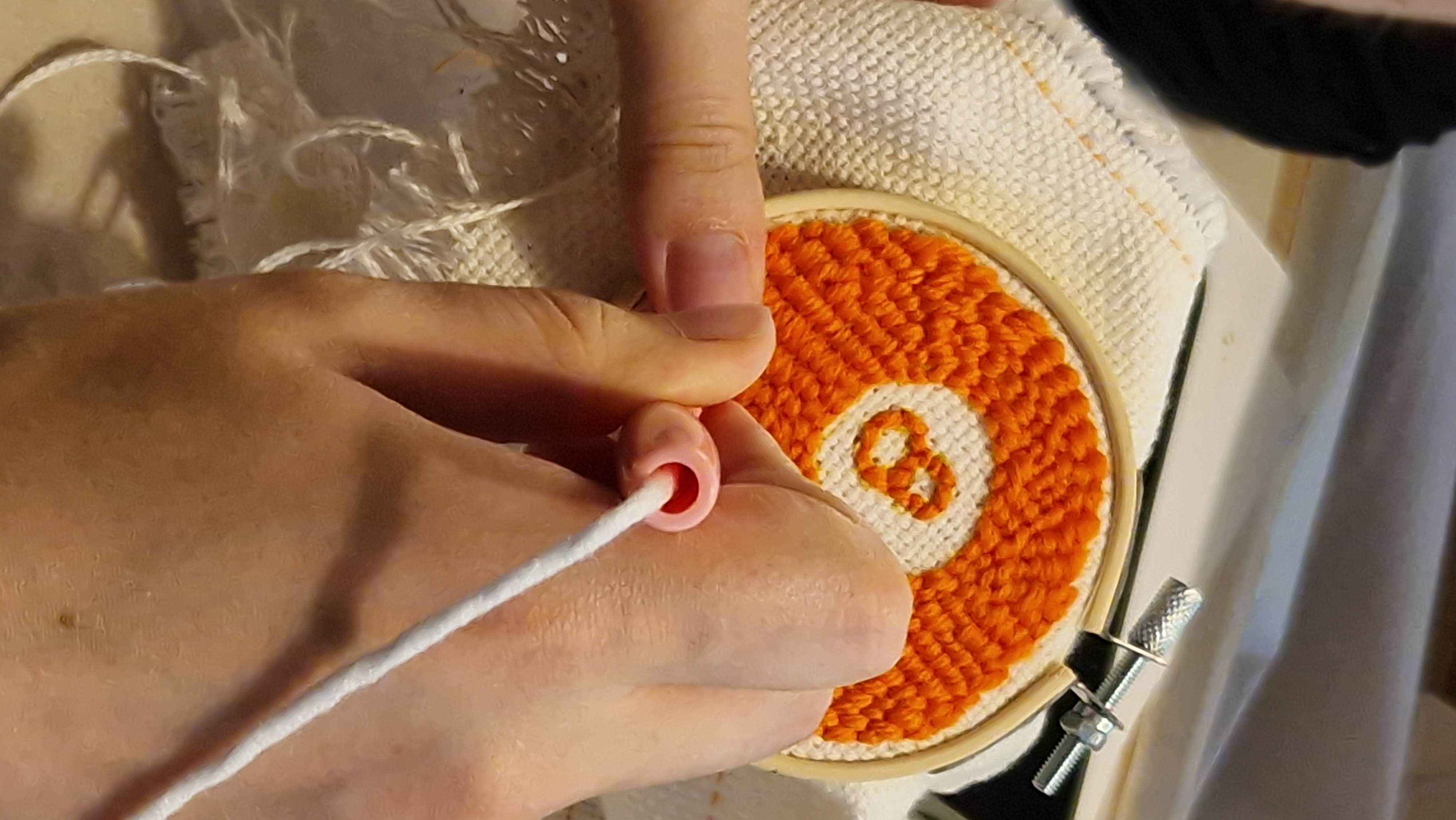 Gros plan punch needle : main, outil et boucles de laine sur le tambour